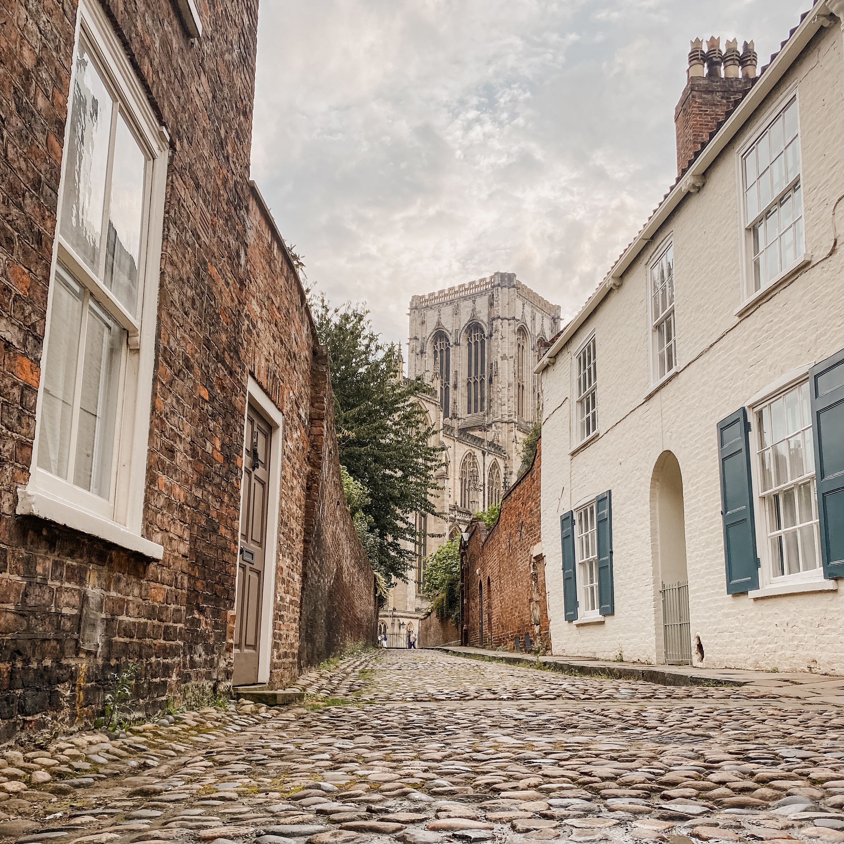 A cobblestone street in York, UK, with a view of the York Minster in the background.