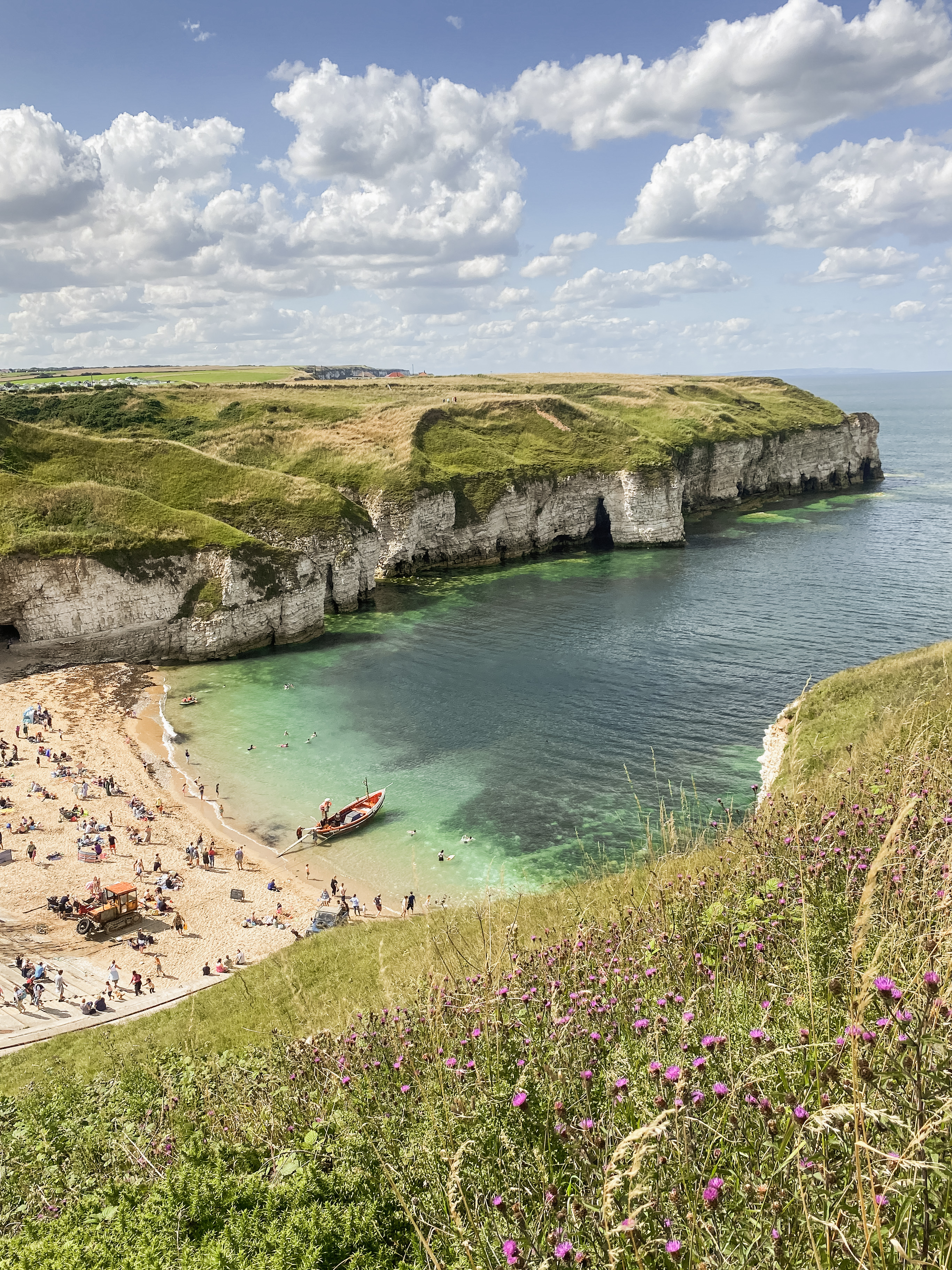 A boat in the water on the Yorkshire coast with people on the beach, clouds against a blue sky